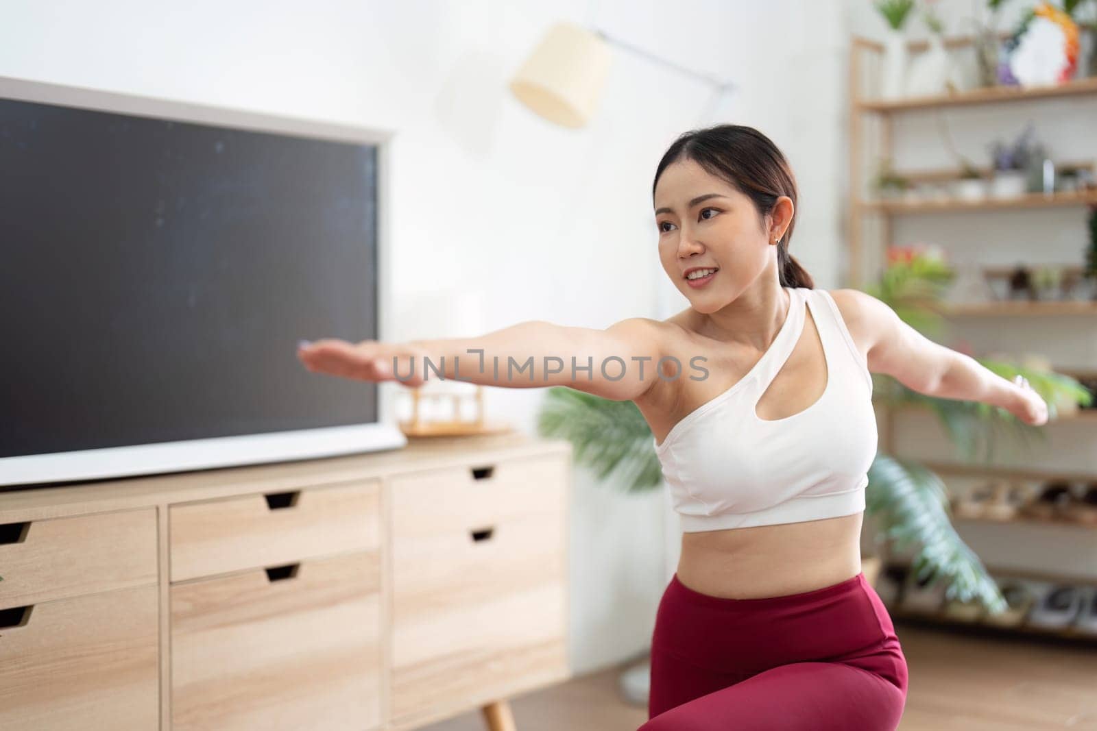 Focusing on her posture, a woman practices yoga, emphasizing both physical strength and mental clarity in a calming environment.