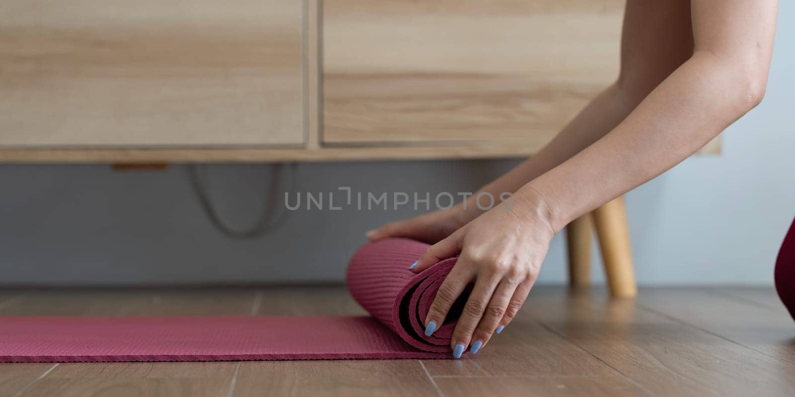 After a calming yoga practice, a woman rolls up her mat, representing peace and focus in her wellness journey.