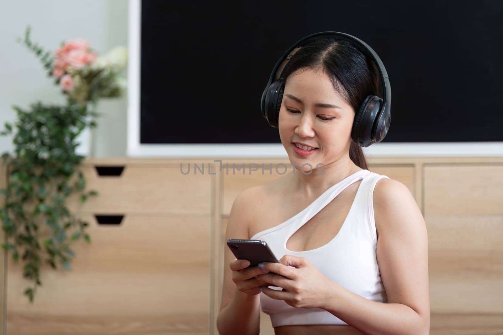 A woman engages with her smartphone while wearing headphones, blending technology with fitness in her daily routine.