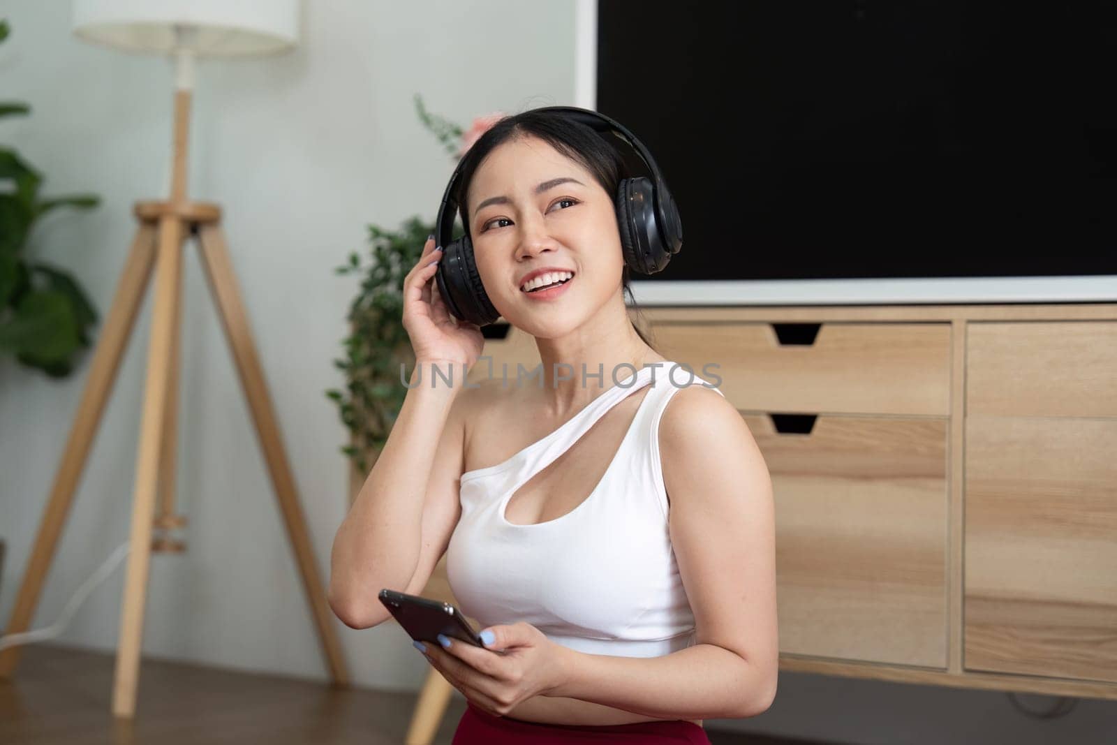 A woman with headphones smiles as she listens to music, embodying wellness through relaxation and enjoyment in her living space.
