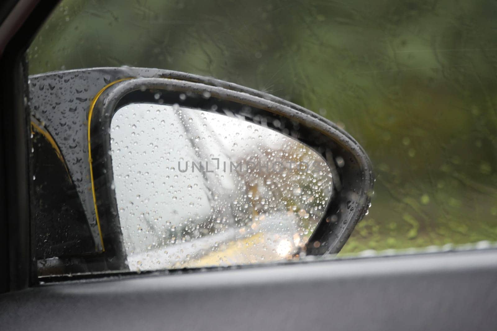 Raindrops collect on the side mirror of a parked car during rainfall.