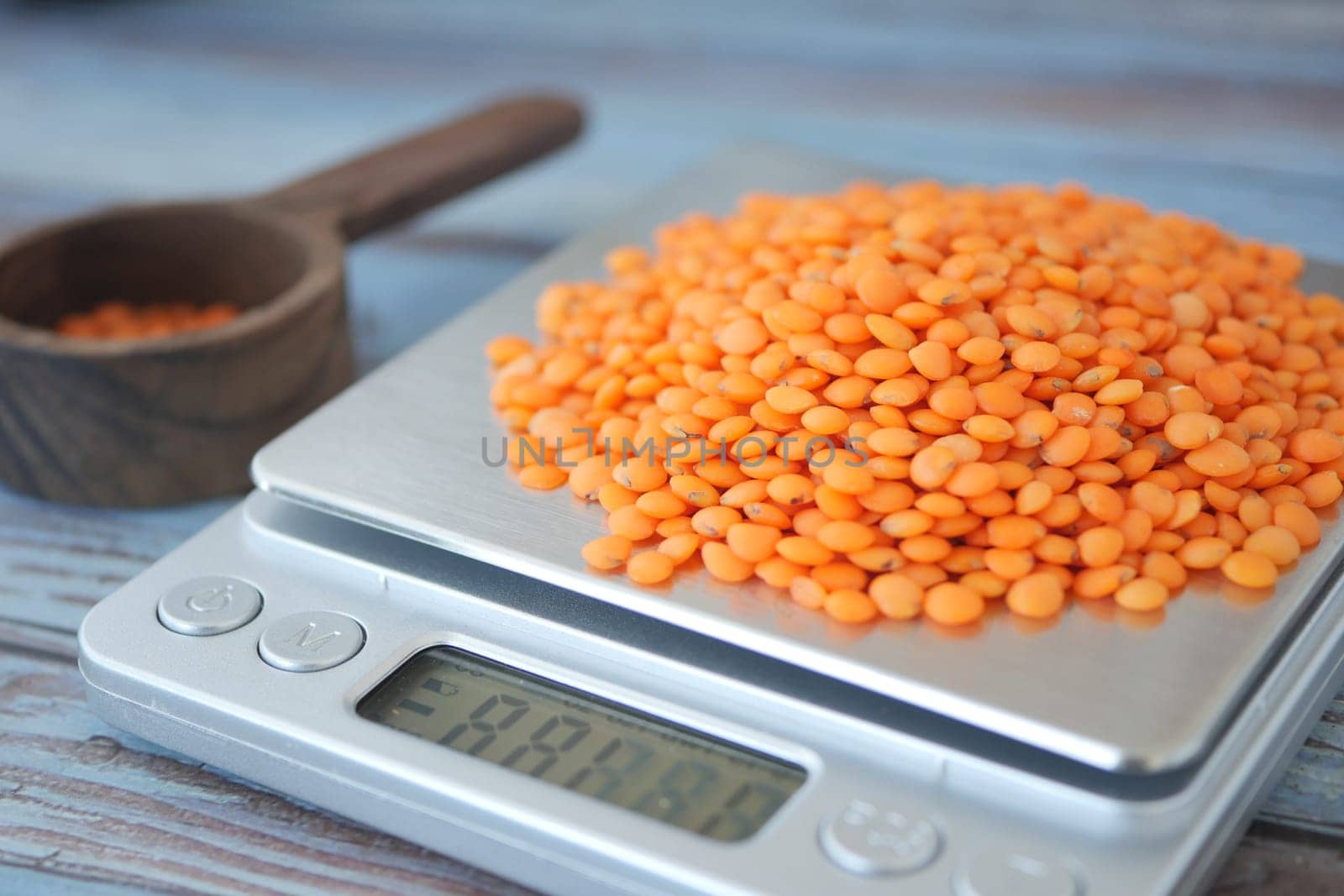 Bright orange lentils pile on a digital scale with a measuring scoop nearby.