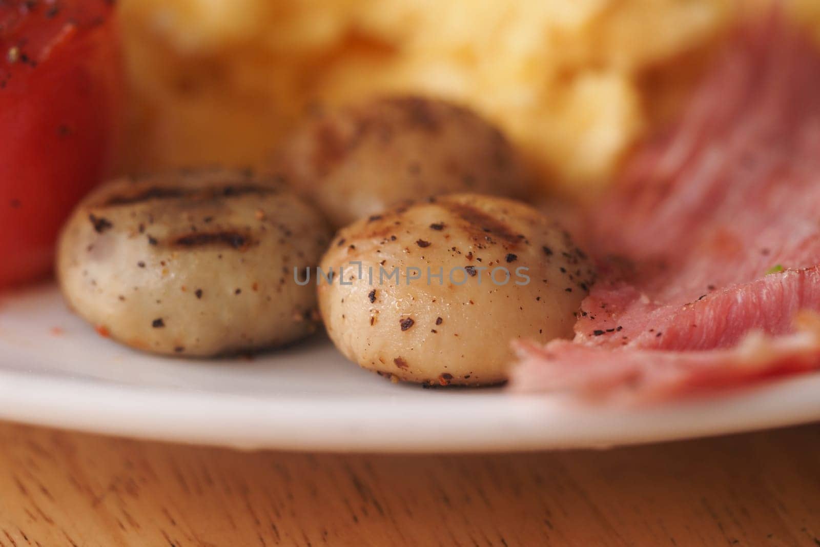 Grilled mushrooms accompanied by ham and fluffy scrambled eggs on a plate.