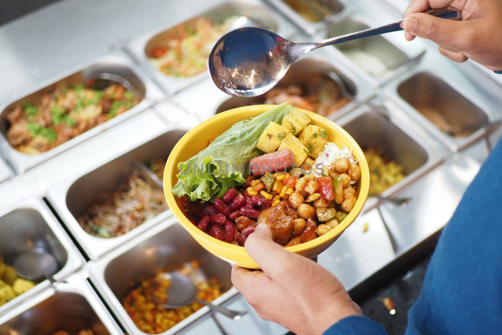 A person holds a bowl filled with vibrant vegetarian ingredients from a buffet.