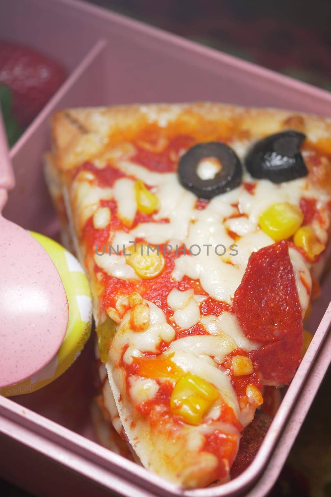 A pizza slice features pepperoni, olives, and corn in a vibrant lunchbox.