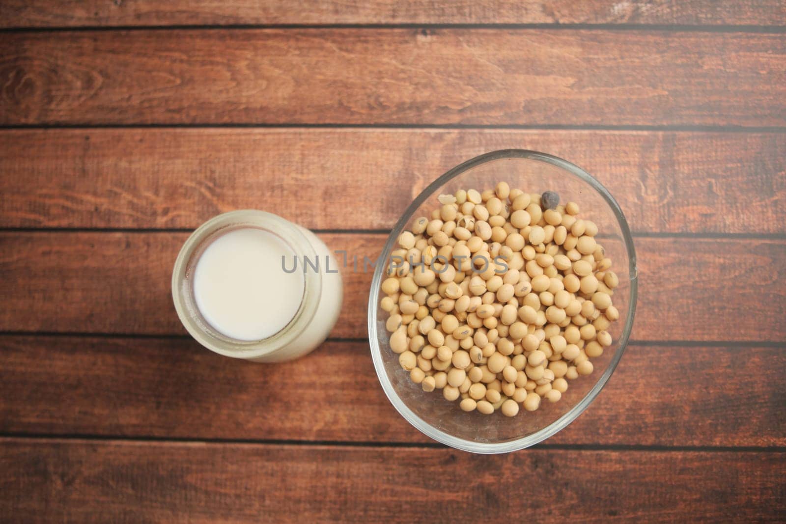 A glass bowl of soybeans alongside a jar of soy milk on a wooden table.