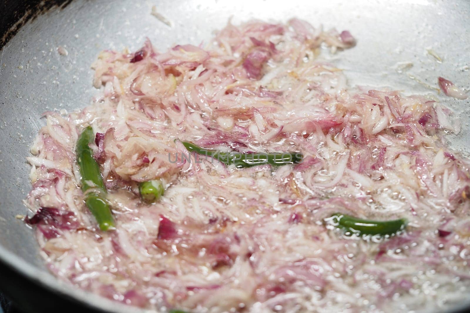 Cooking sliced onions and green chilies in a pan on the stove.