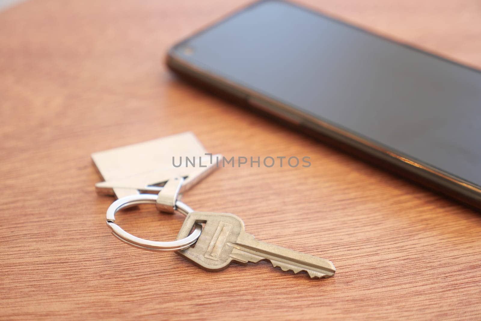 Keys rest next to a sleek smartphone on a warm wooden table.