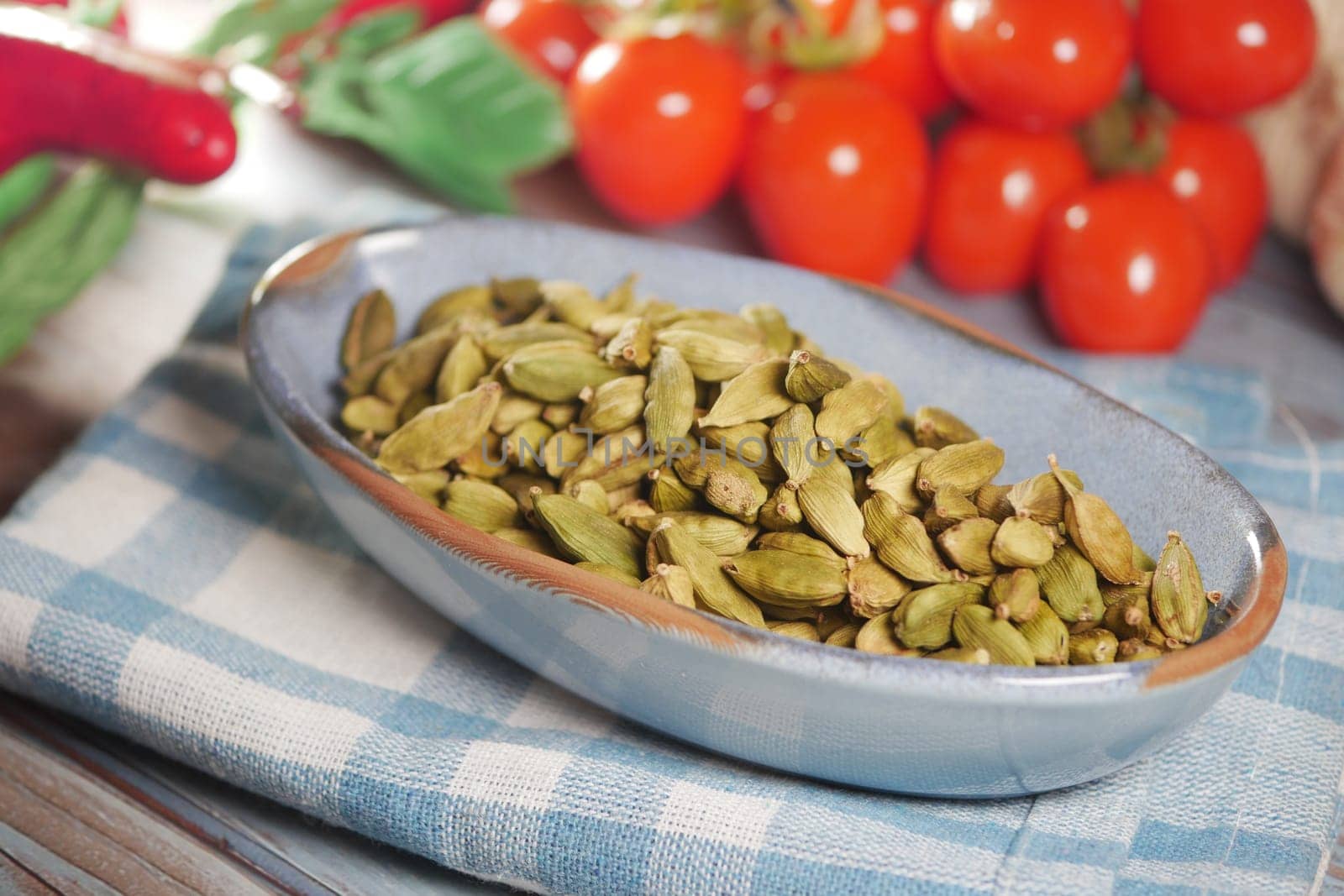 Green cardamom pods are arranged in a bowl alongside ripe tomatoes.