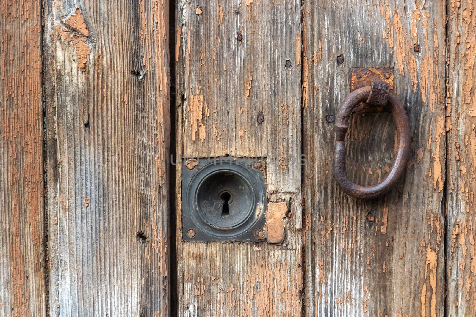 Vintage crackled- chipping paint wooden outside door, weathered and peeled by time background with a old metal knocker and key hole