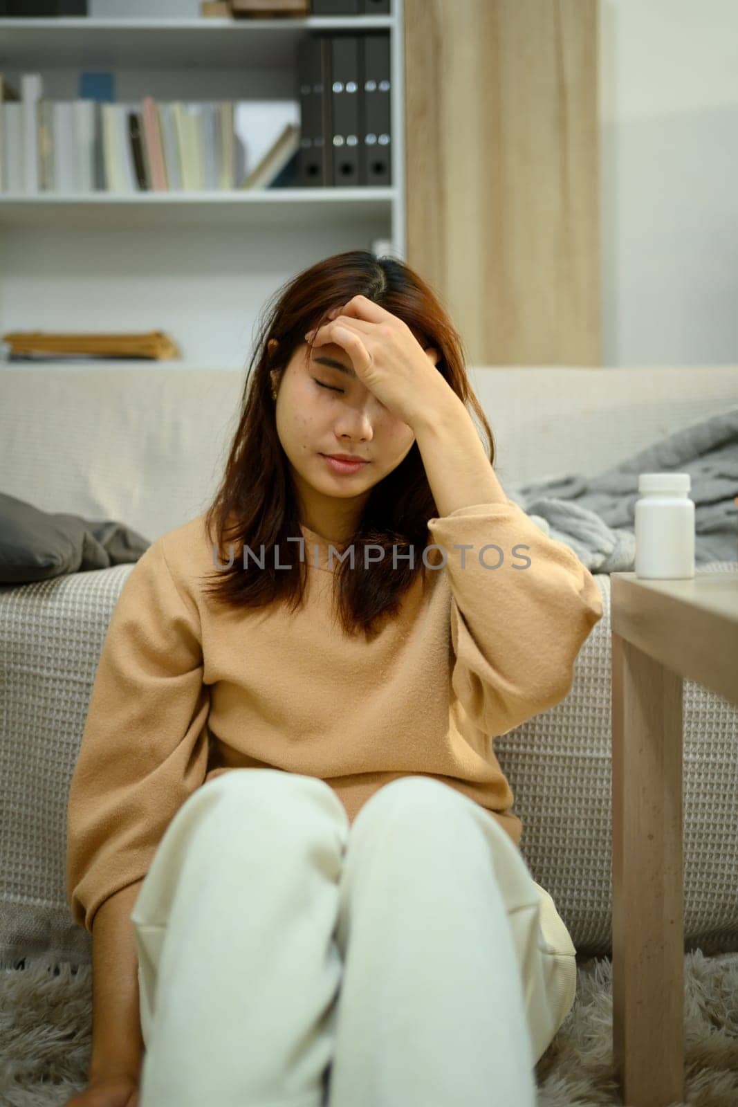 Young woman sitting on the floor with hand on her forehead. Health, wellness or mental exhaustion concepts.
