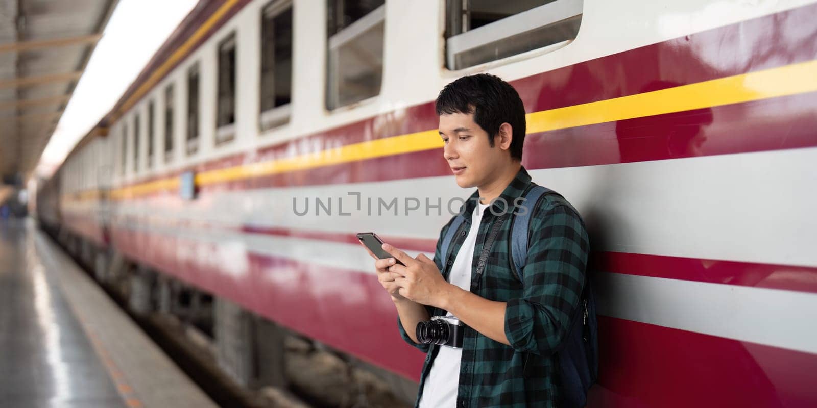 Standing next to a vibrant train, a young traveler interacts with his mobile device, illustrating the fusion of travel and technology in the modern age.