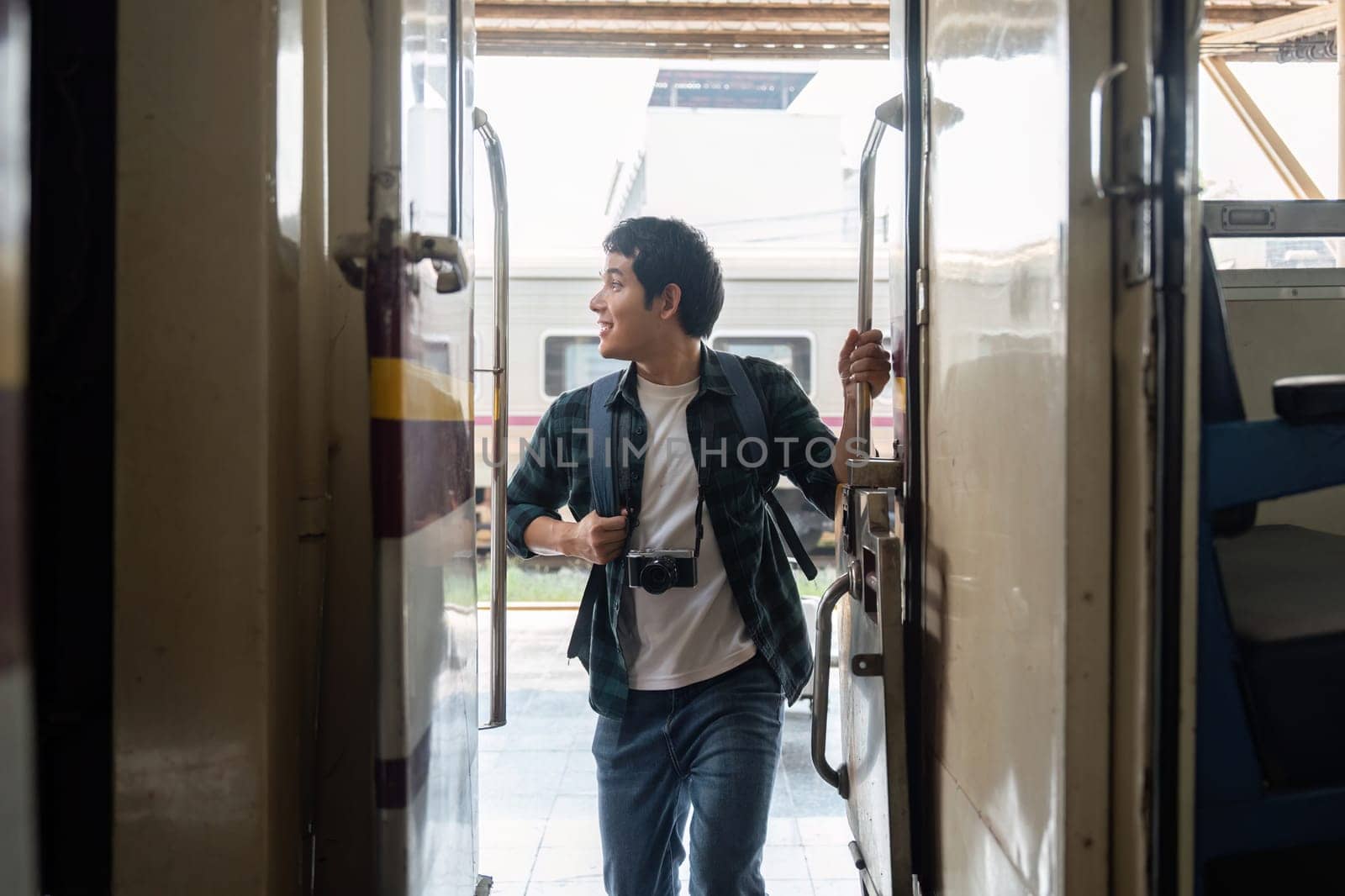 A young man opens the train door and steps inside, looking back with a joyful expression. His camera signifies that he is ready to capture moments during his adventure.