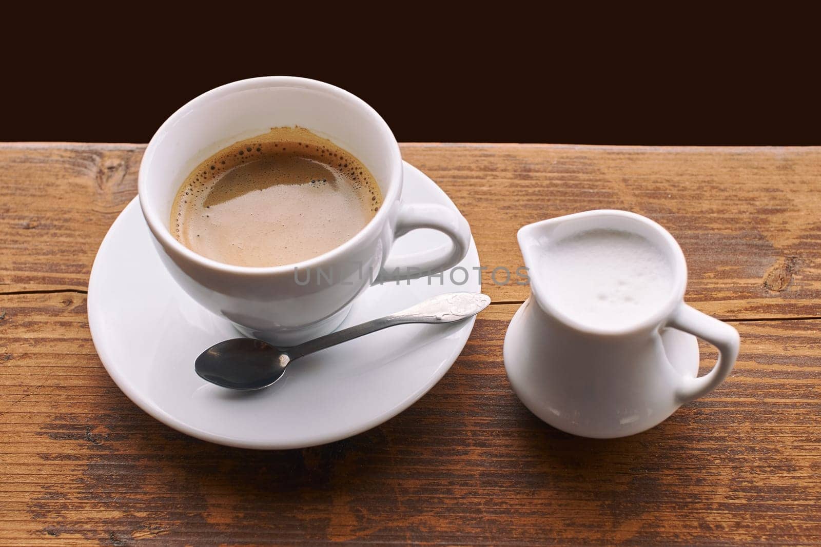 Coffee with milk in ceramic cup with small milk jug