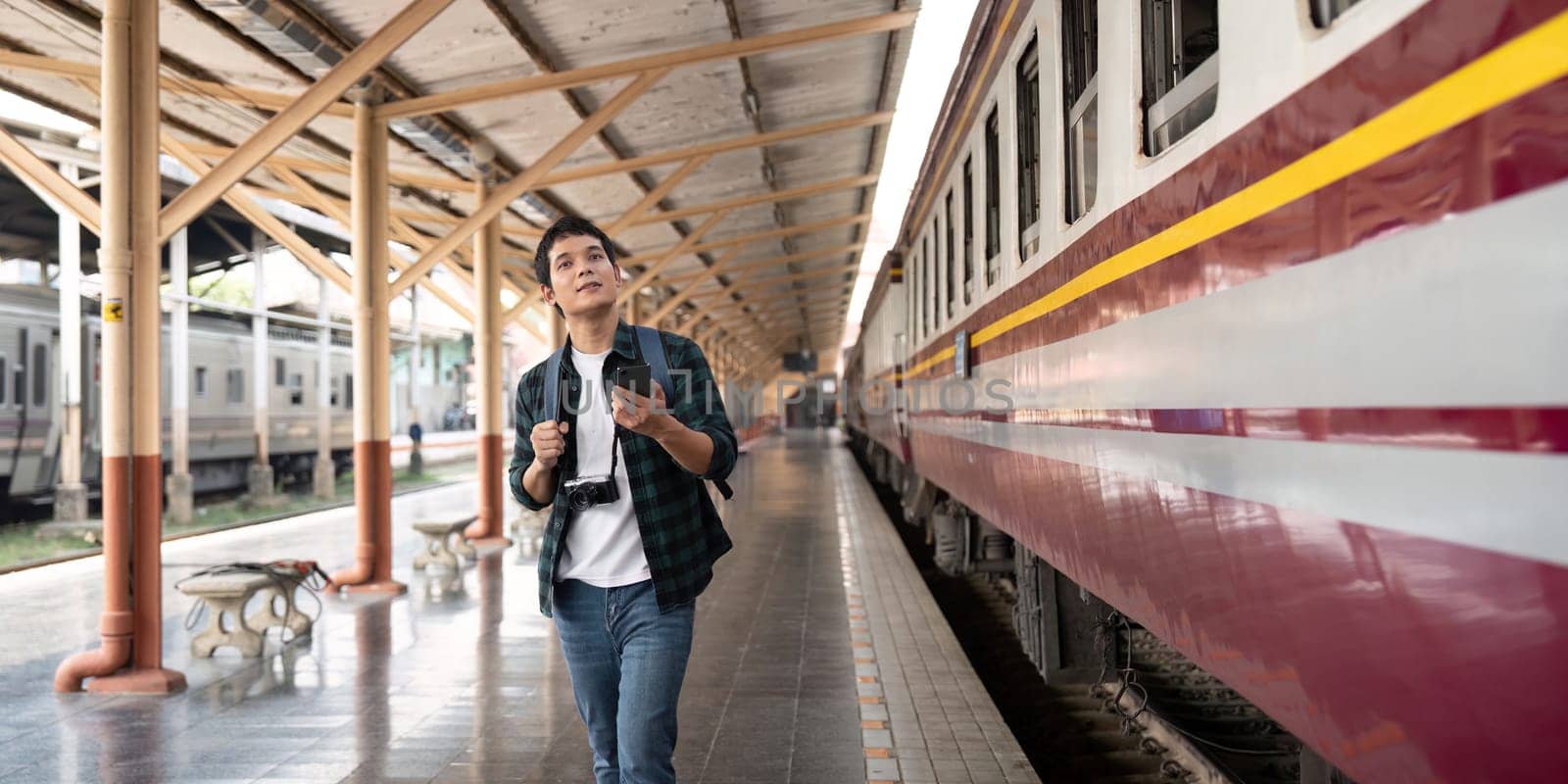 A young man walks through an empty train station, examining his surroundings with curiosity and anticipation. His camera adds to the excitement of his upcoming travel plans.
