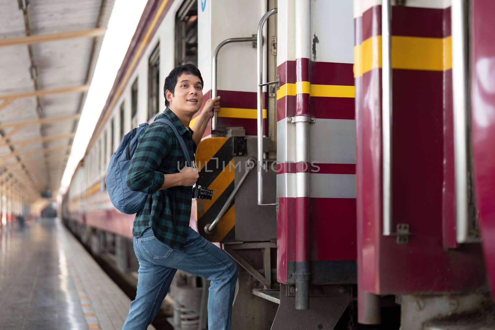 Excited for his next adventure, a young man prepares to board a train, highlighting the thrill of travel and the journey ahead with his camera in tow.