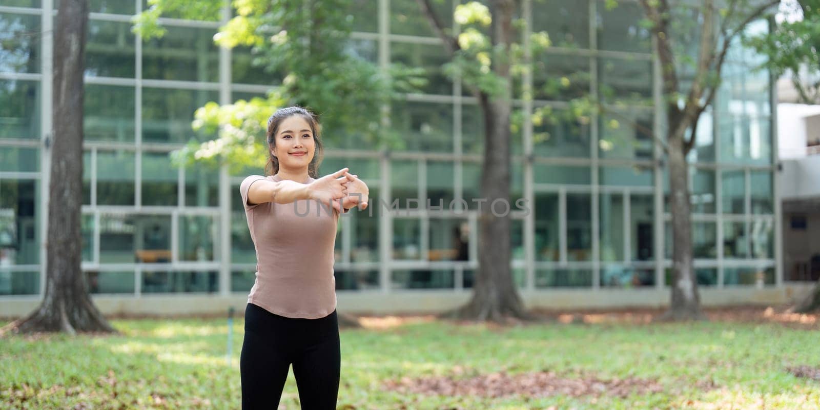 Focused on her fitness journey, a woman stretches her arms outdoors, promoting her health and well-being while integrating nature into her workout routine.