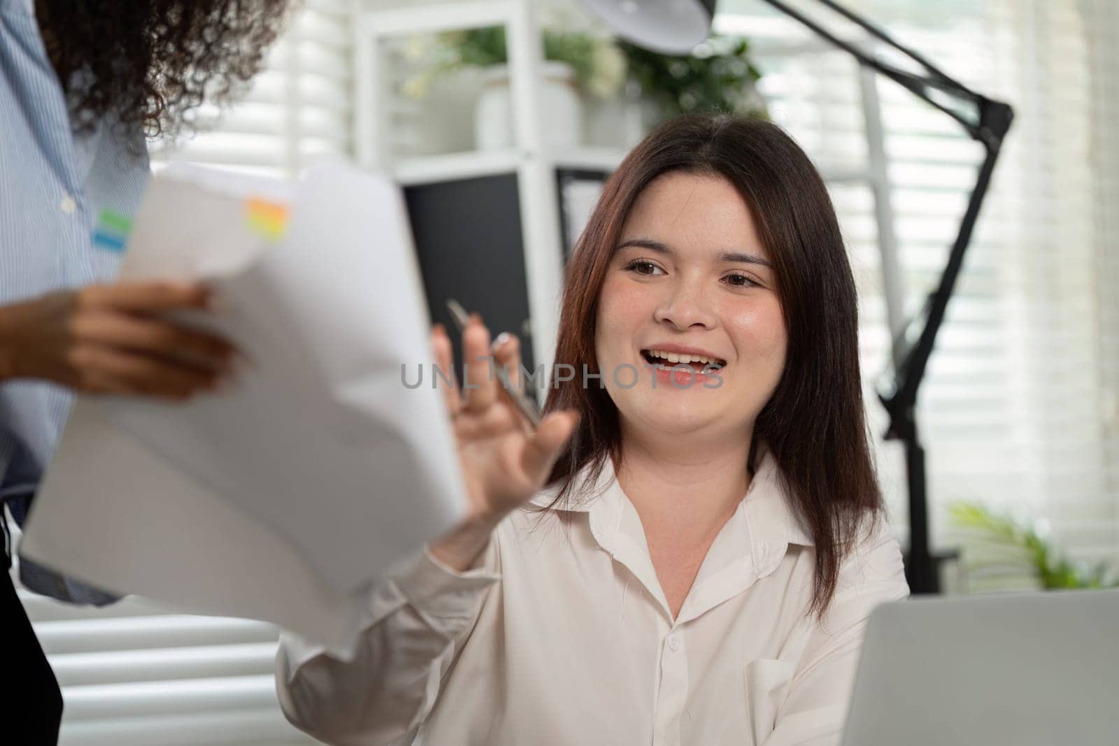 Two coworkers engage in collaborative brainstorming over documents and a laptop, enhancing creativity and teamwork in a modern office setting.