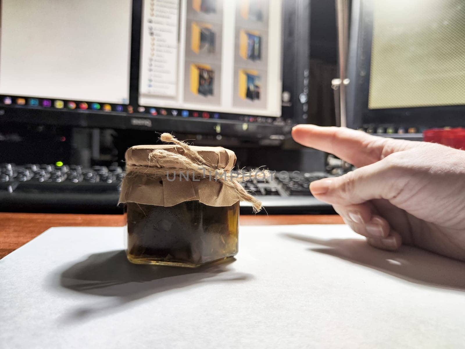 Individual browsing online purchases at a desk, highlighting a jar in the foreground. Screens show various items.