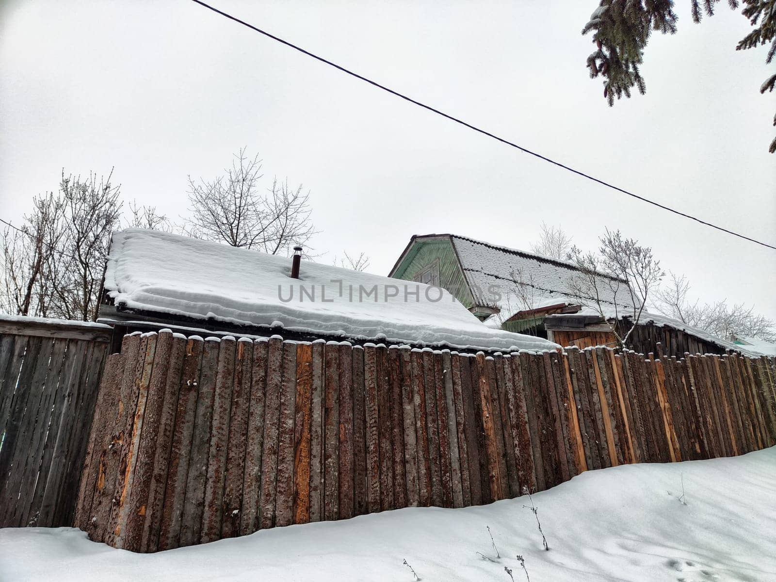 Snow blankets traditional structures and a wooden fence, capturing the tranquility of a winter day.