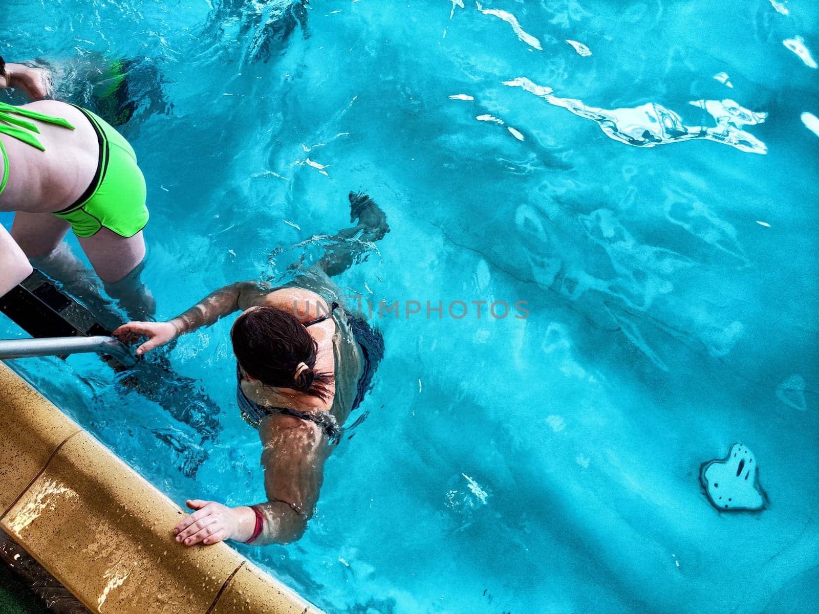 Individuals are swimming and engaging playfully in a bright indoor pool while enjoying a sunny afternoon together.