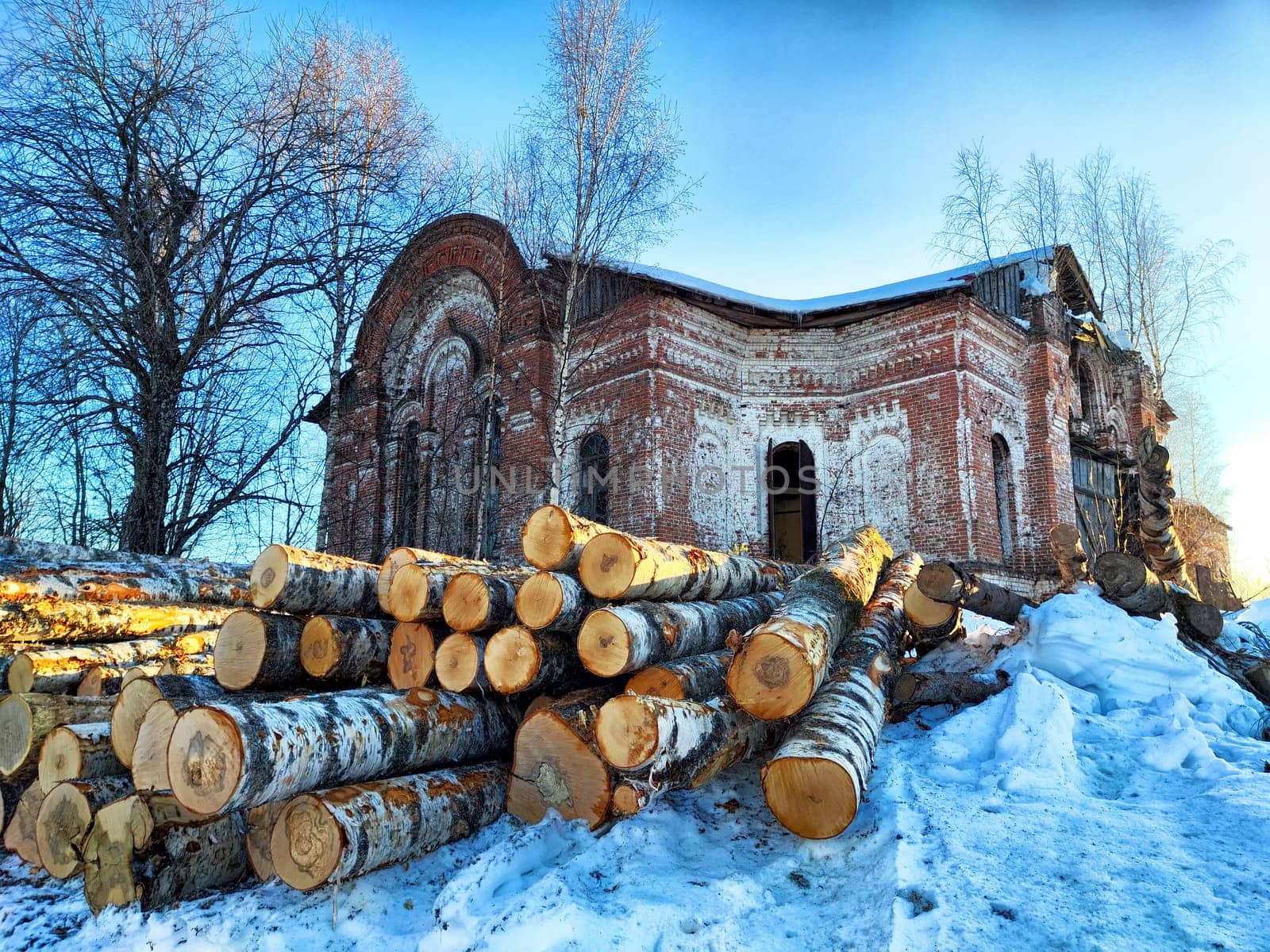 Snow-covered ground presents a backdrop for a brick structure amidst neatly stacked logs, reflecting a tranquil winter day.