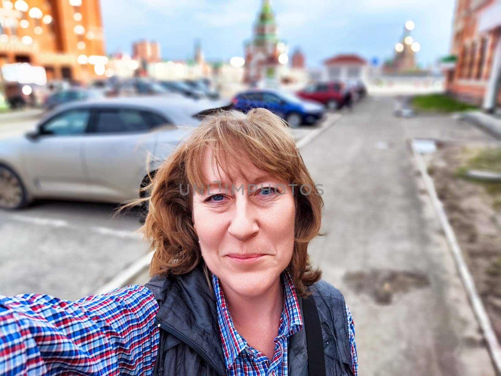 A middle-aged female traveler blogger captures a selfie in a vibrant city, showcasing her adventurous spirit.