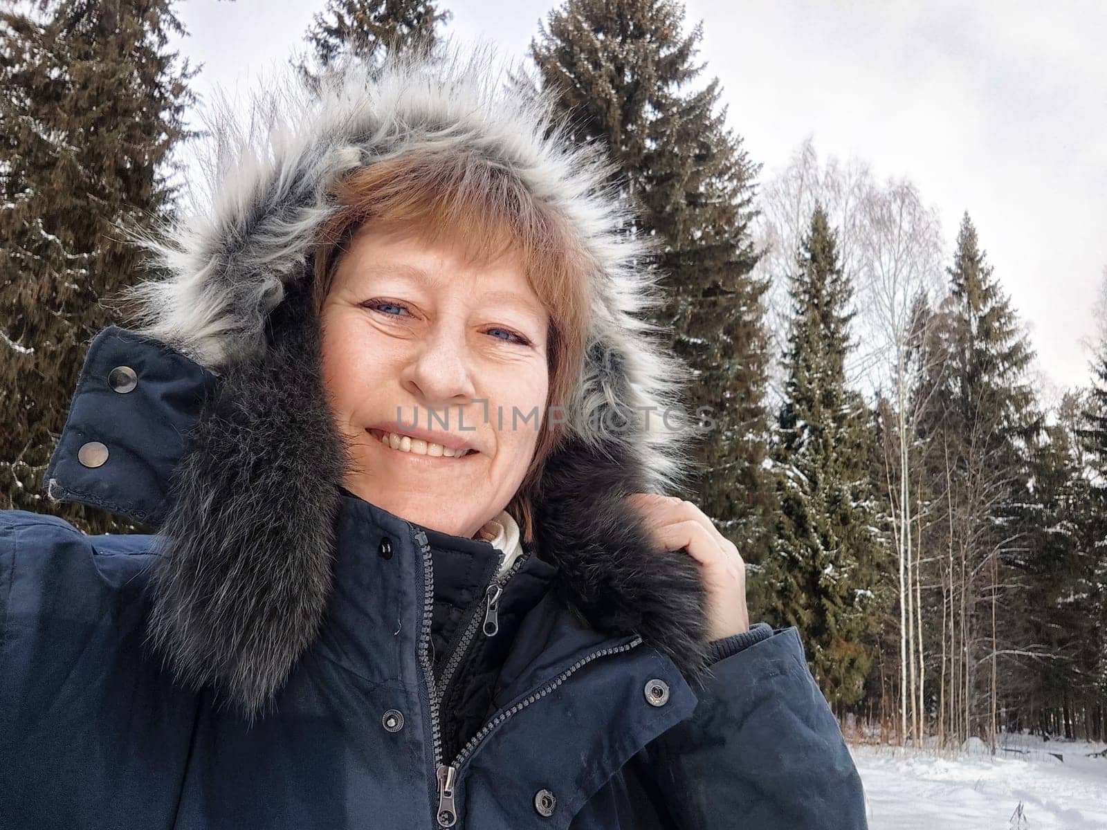 Smiling woman takes a selfie in a snow-covered forest while exploring nature and enjoying her winter trip.