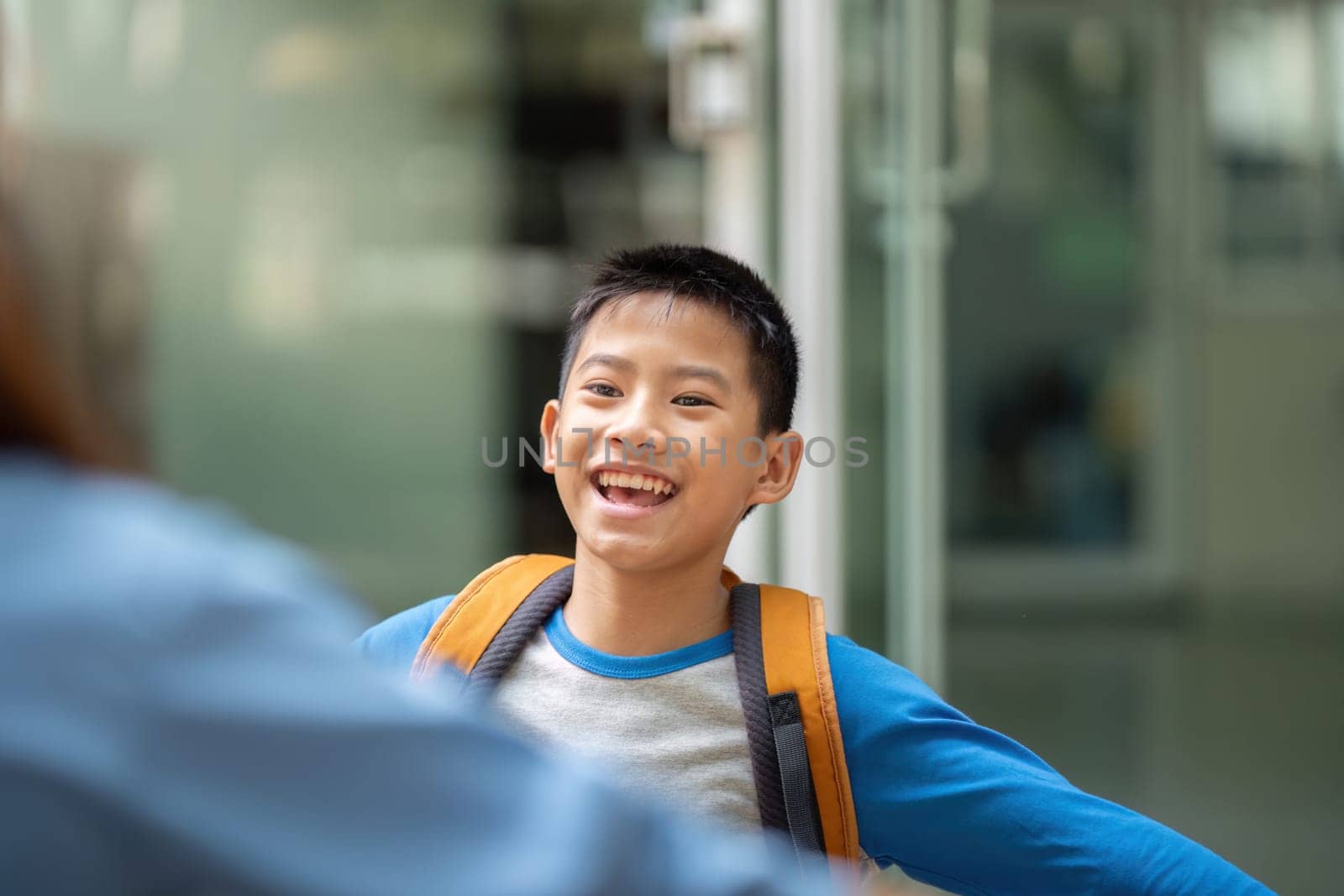 A smiling boy joyfully opens his arms as he reunites with his mother after school, showcasing their close relationship and love.