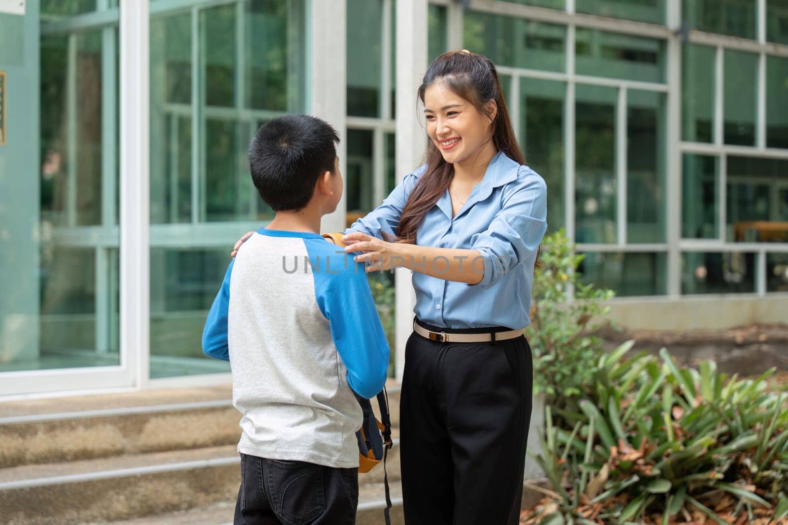The mother kneels to embrace her son, preparing him for his school day. Their connection illustrates the support and love in their relationship.