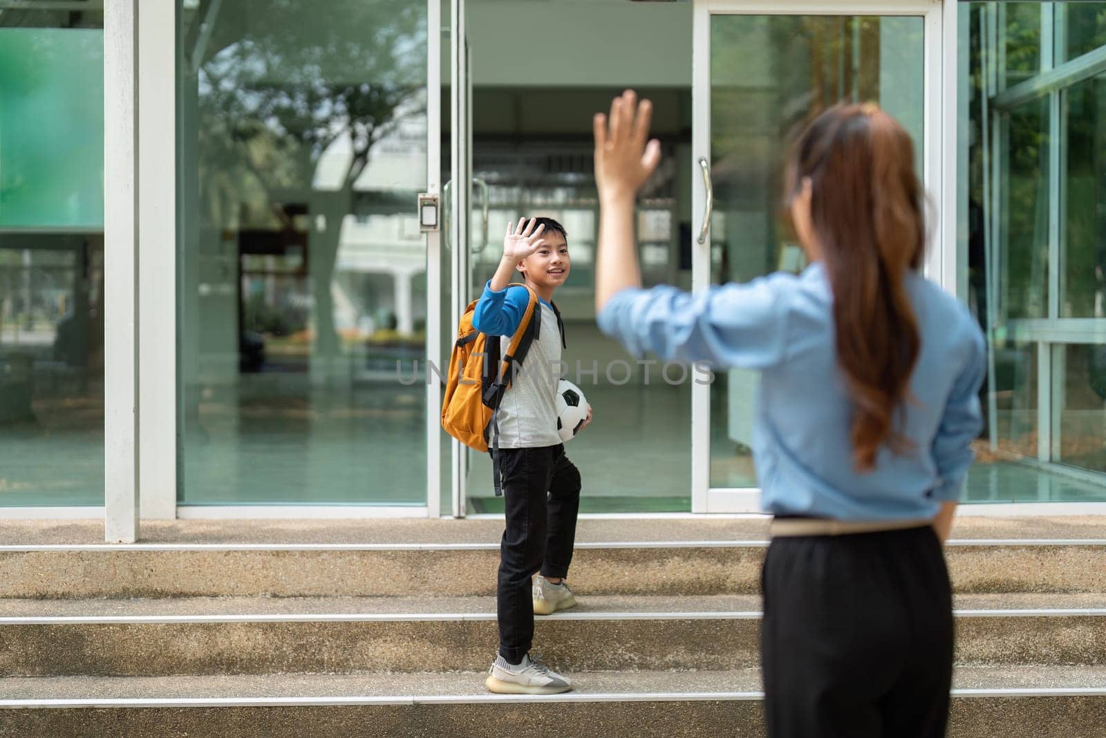 As her son waves back at her, a sense of pride fills the mother's heart, highlighting their close relationship as he heads confidently to school.
