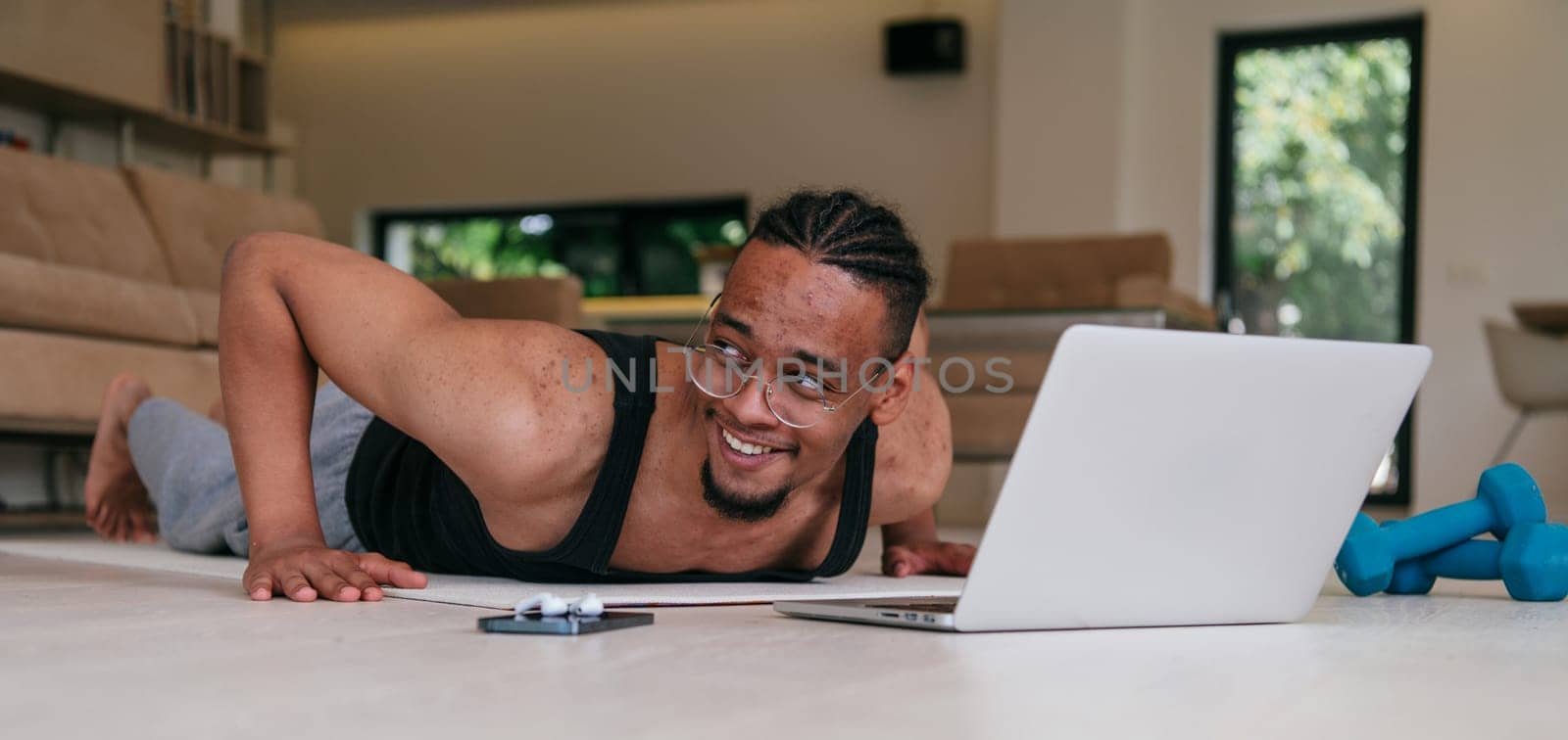 Training At Home. Sporty african american man doing the training while watching an online tutorial on a laptop, exercising in the living room, free space.