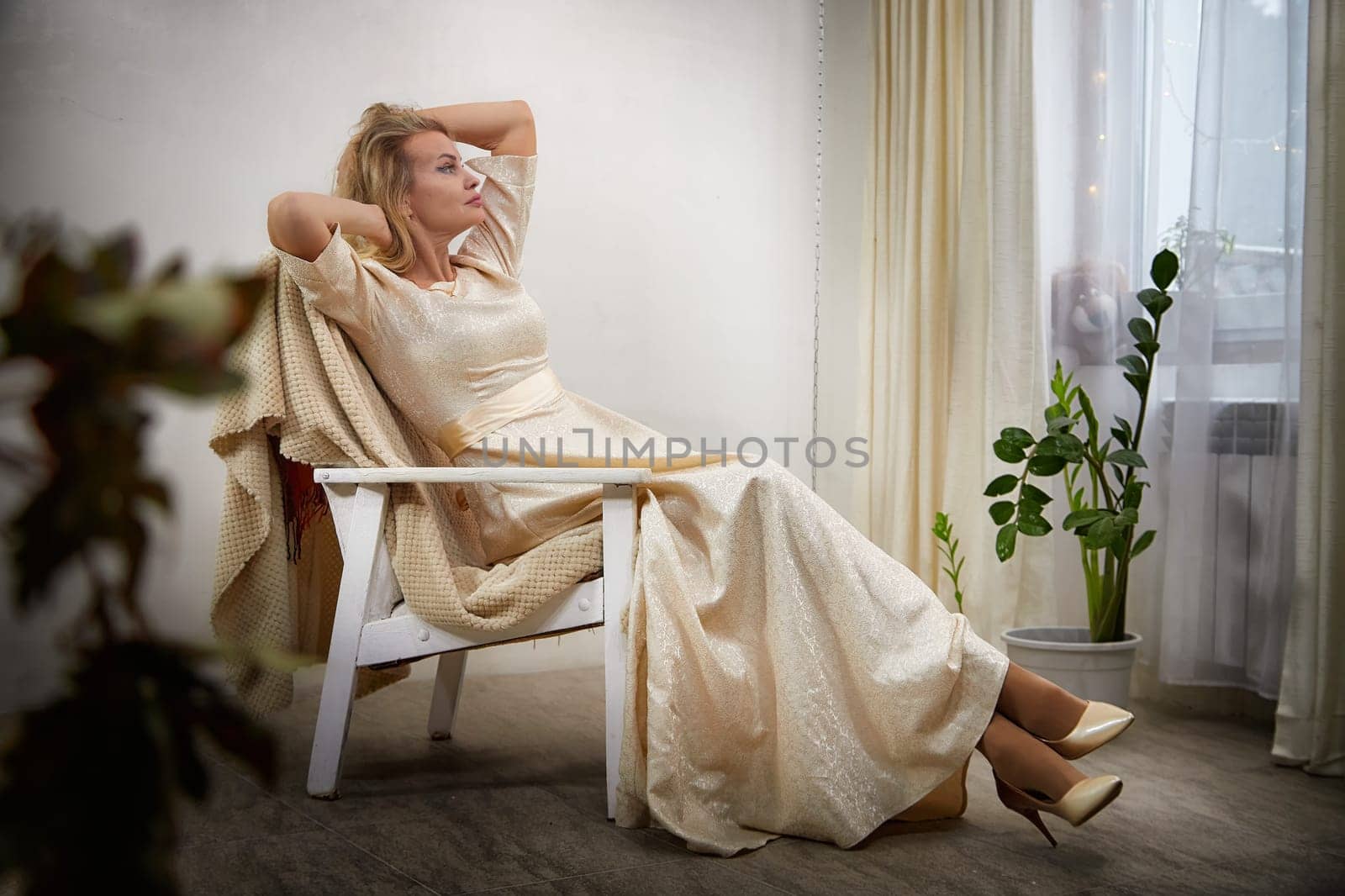 A middle-aged blogger poses stylishly in a stunning dress while capturing content in her cozy indoor space.