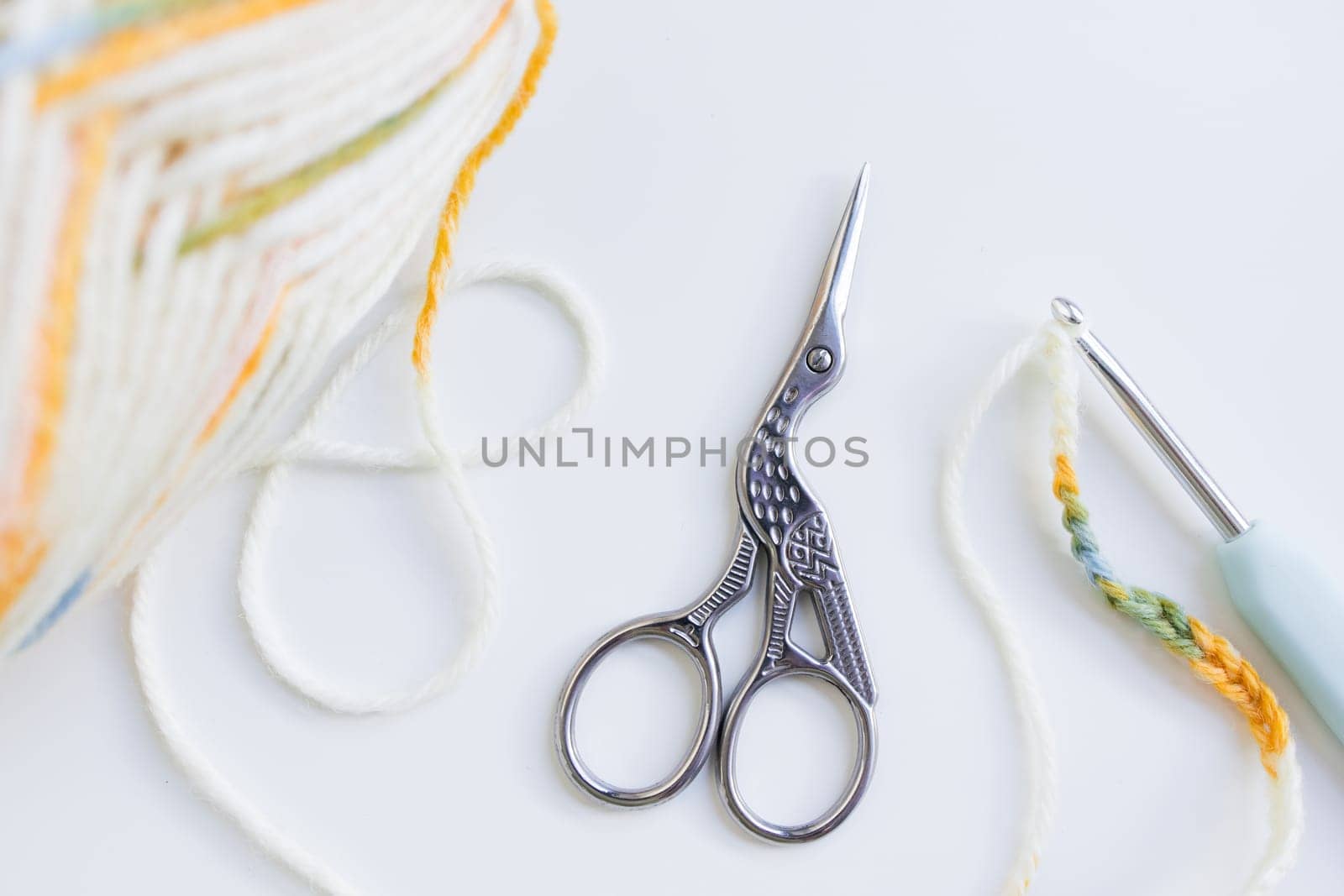 Crochet tools and yarn ball with bird shaped scissors on white surface.