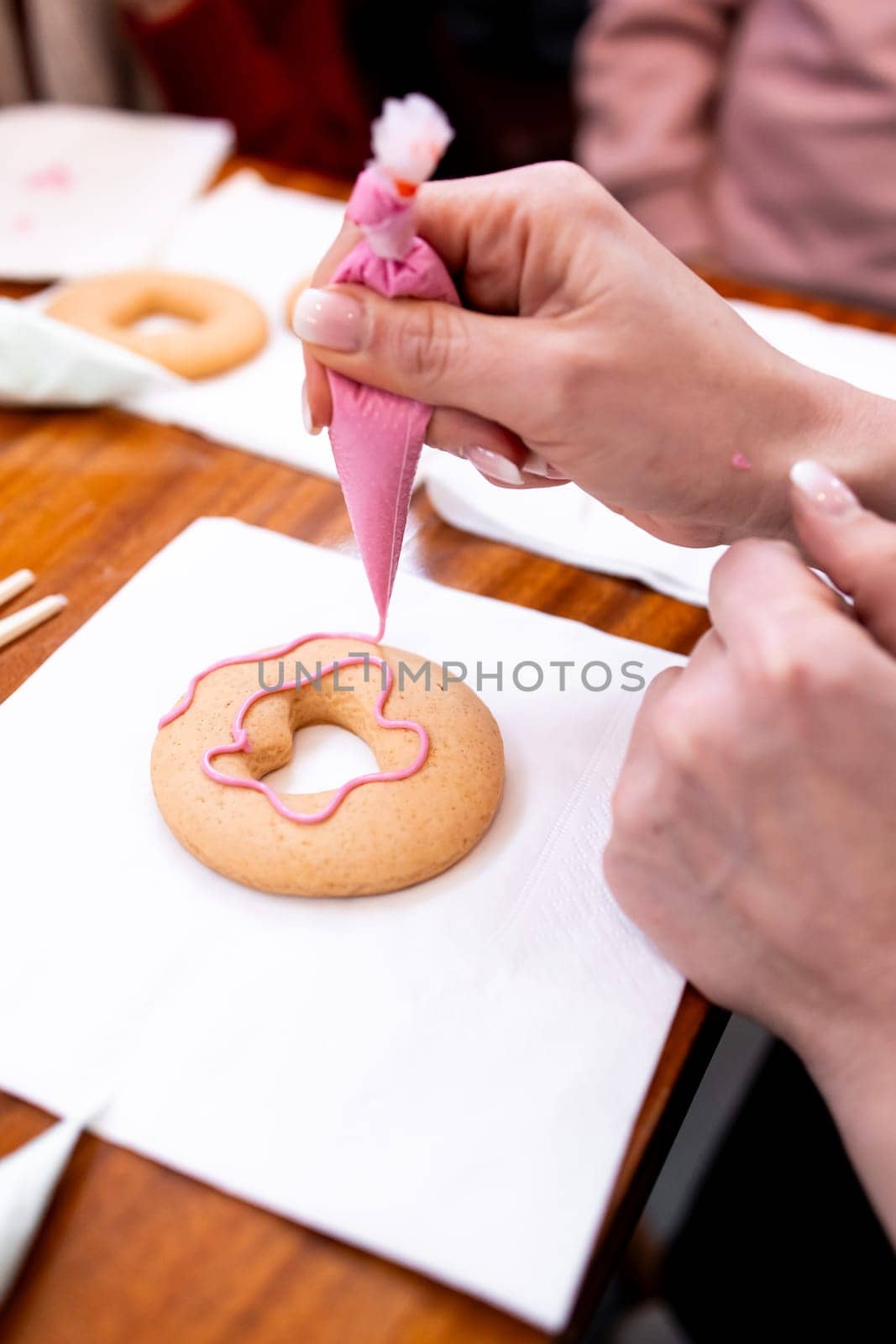 Person icing heart shaped cookie with pink frosting on wooden table.