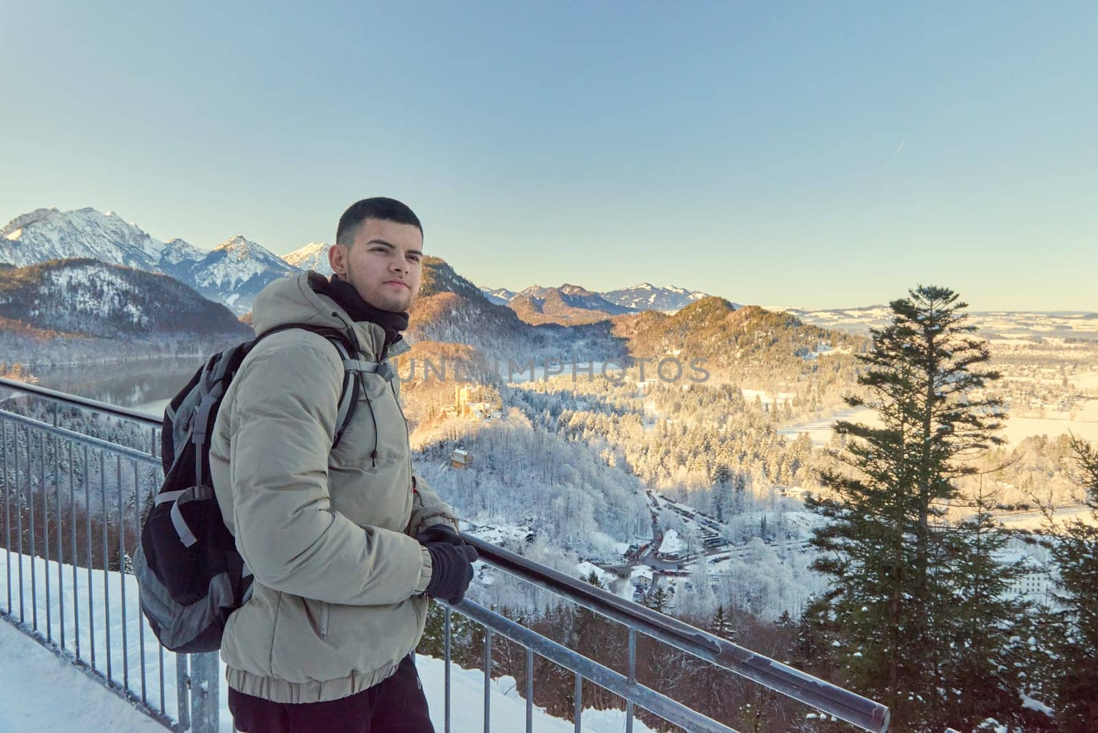Man standing on a balcony with scenic mountain background, capturing a serene winter scene with icy mountains and forest in the background