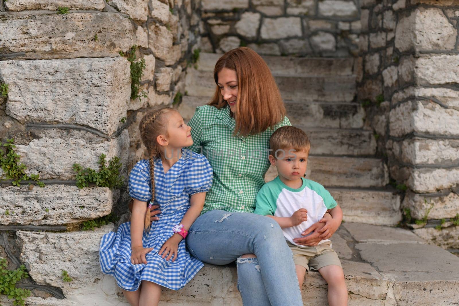 Mother hugs son and daughter and smiles near stone wall
