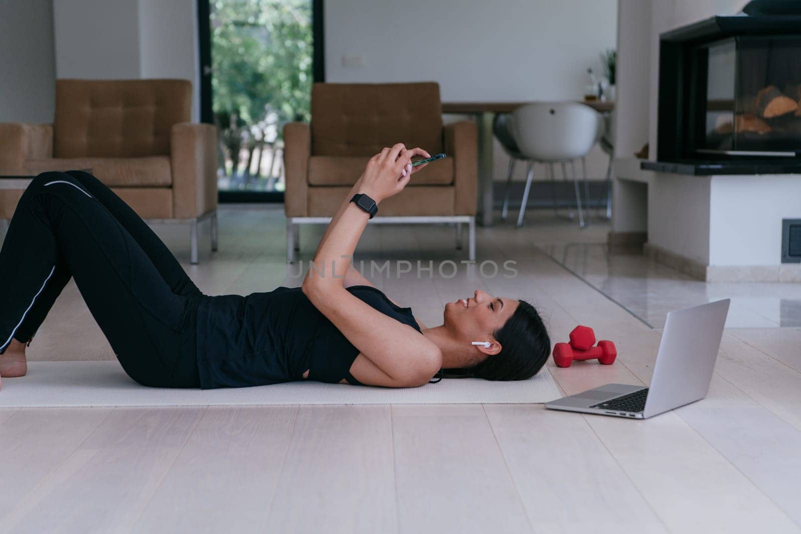 A sportswoman using a smartphone while resting and lying on the modern house floor.