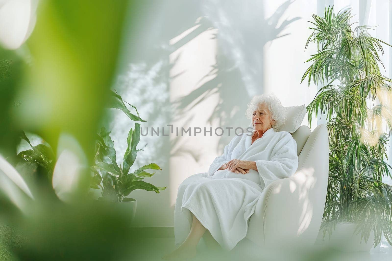 An elderly woman sits peacefully in a lounge chair, dressed in a white robe, her hands folded gently in her lap.
