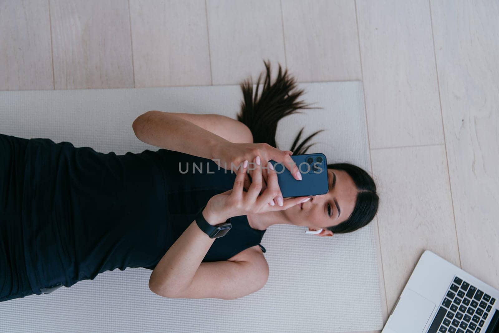 Sportswoman using a smartphone while resting and lying on the floor of modern house