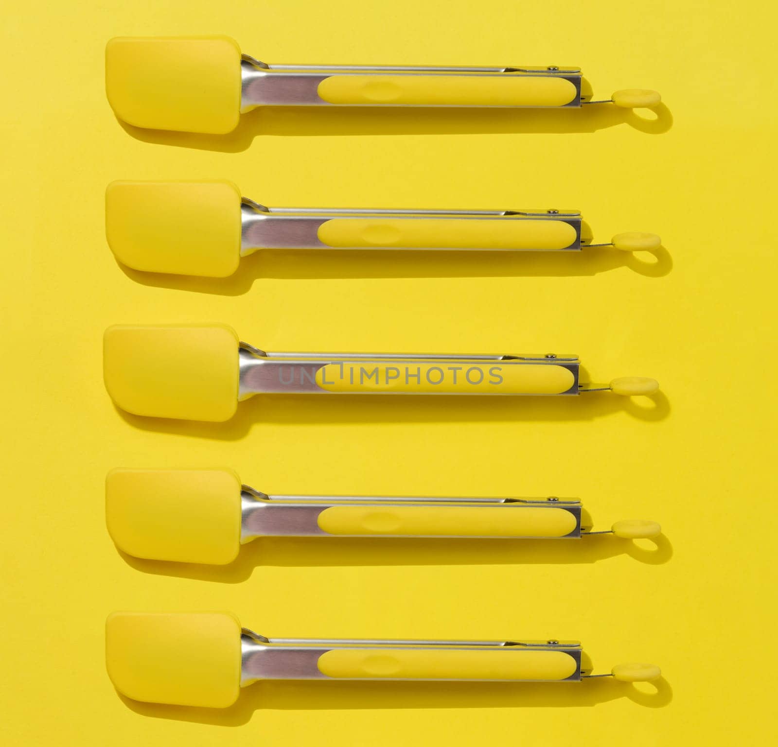 Yellow kitchen tongs with shadow on yellow background, top view