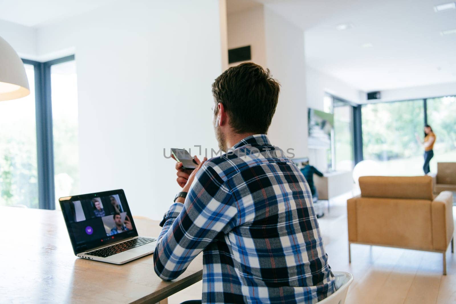A freelancer sitting at a table in a modern living room, with headphones using a laptop for business video chat, conversation with friends and entertainment.