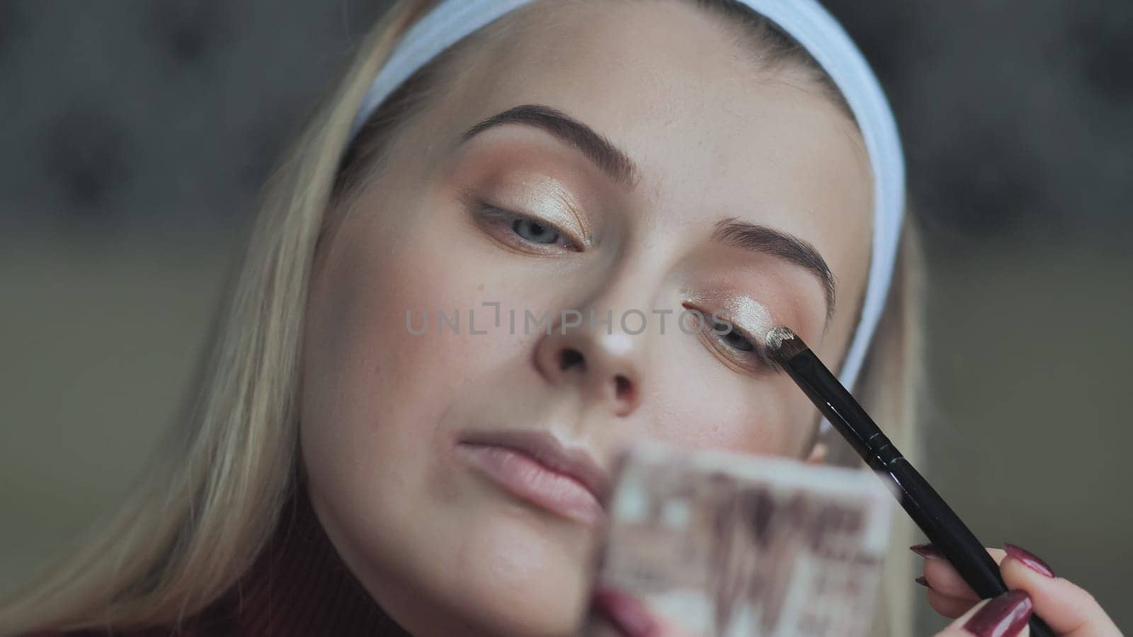 A blonde girl applies makeup to her eyelids