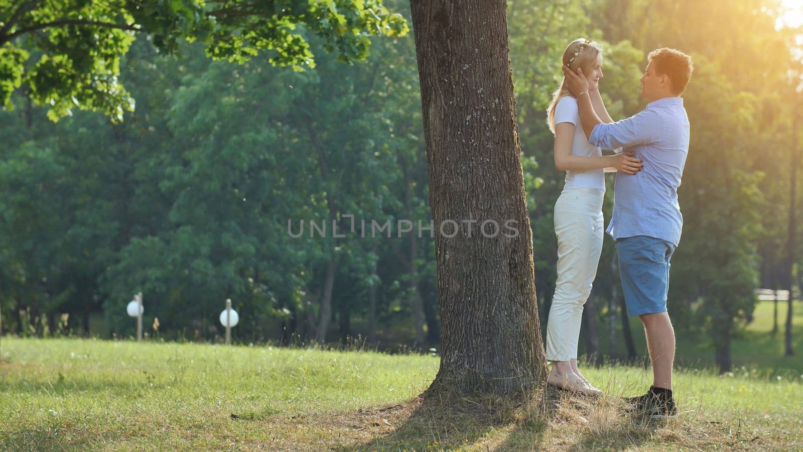 A young man and woman are standing under a tree in a park and hugging