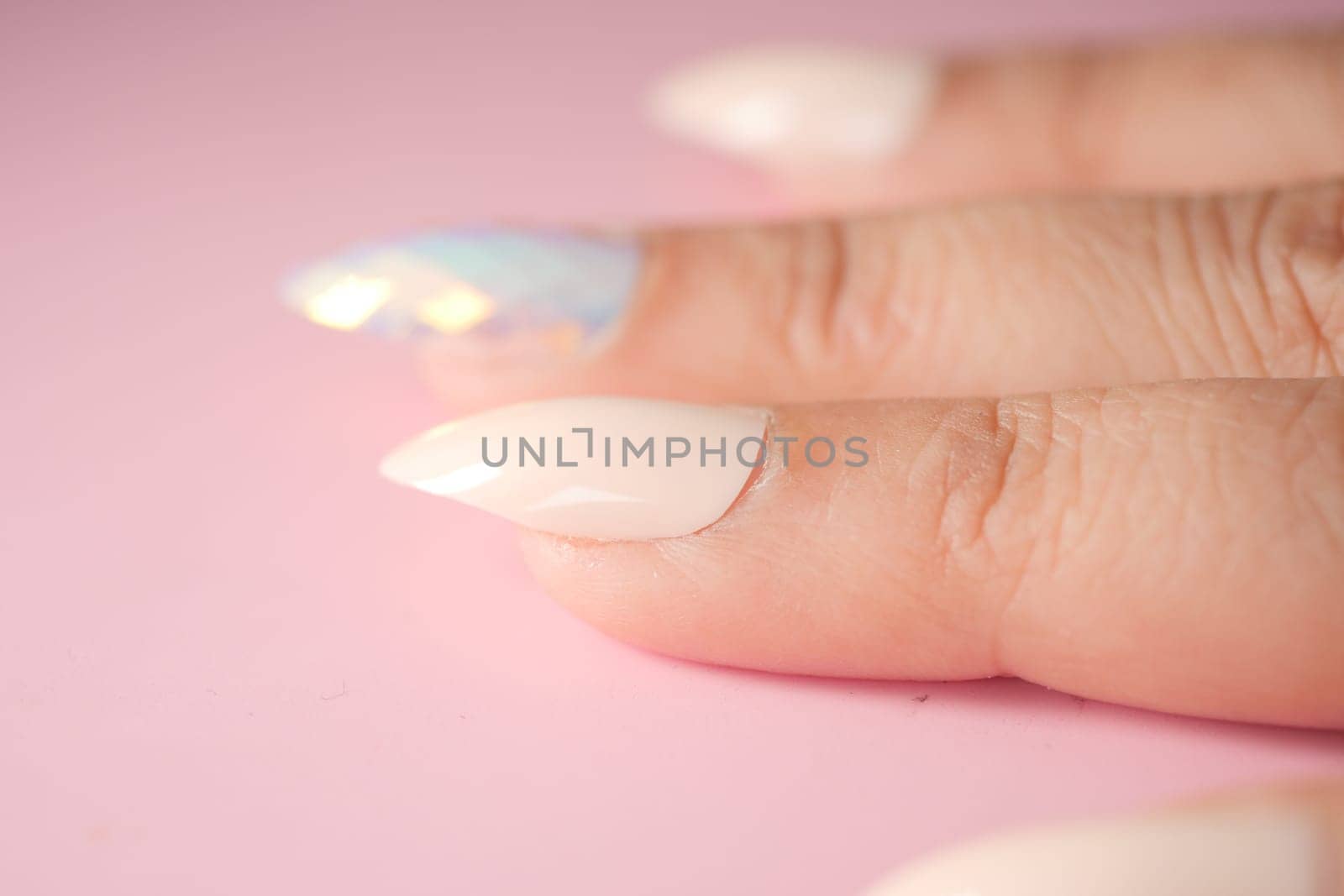 Intricate nail art showcases white and shimmering colors on fingers.