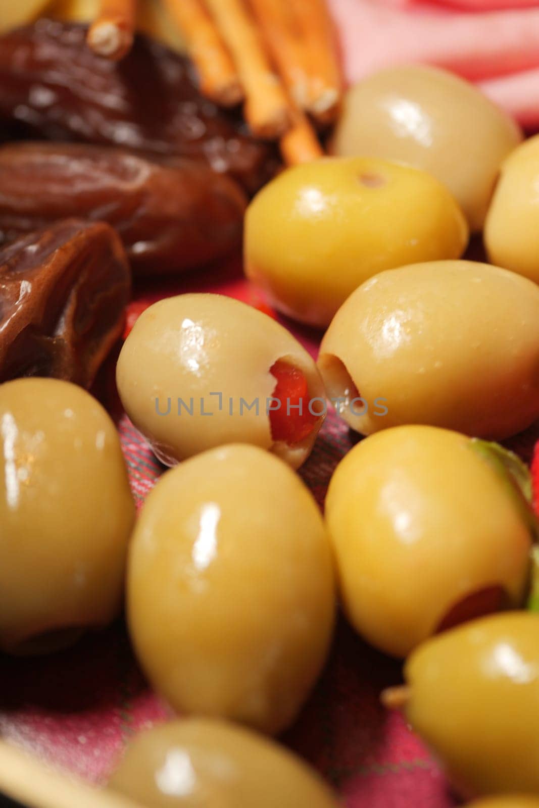 Green olives filled with red pimentos alongside dried fruits on a plate.