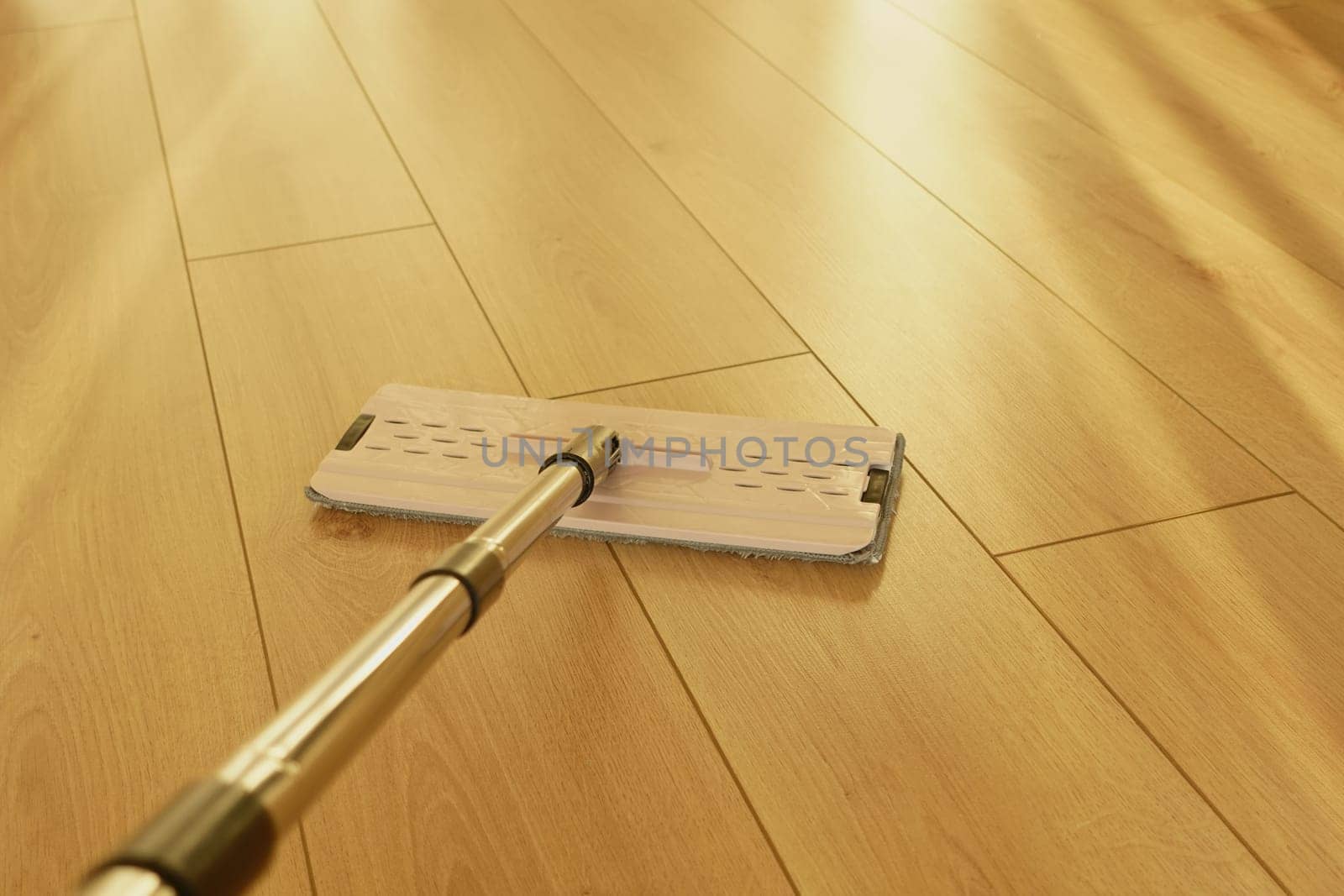 A person is mopping a wooden floor on a sunny afternoon.