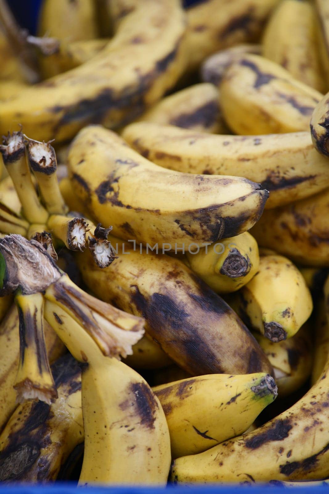 Bananas with brown spots fill a market stall in the afternoon light.