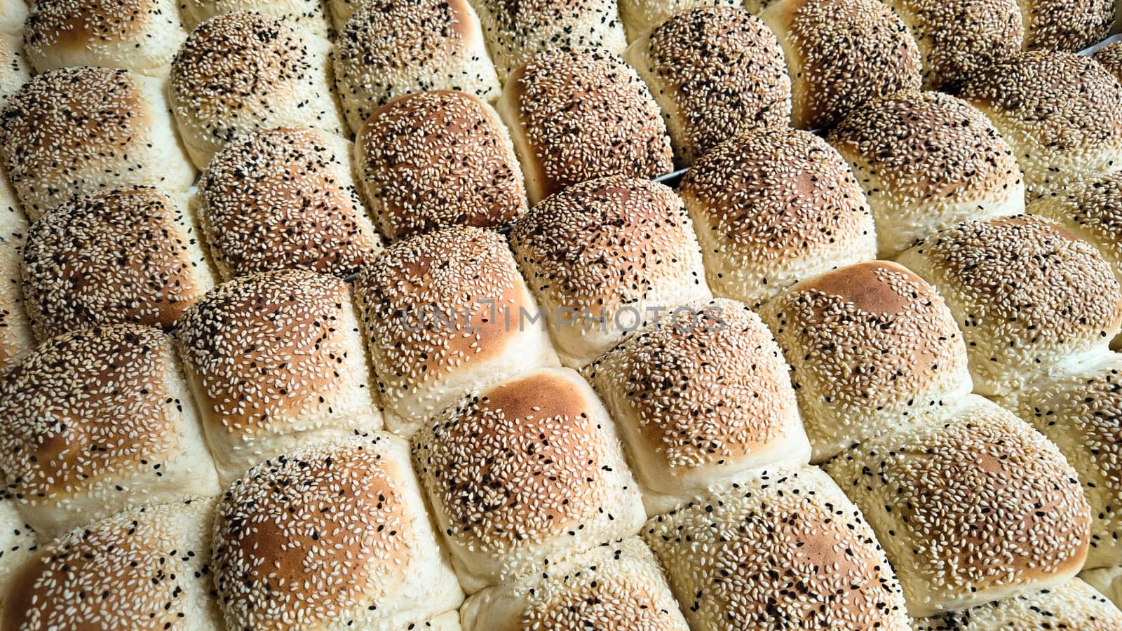 Warm and fluffy sesame seed rolls are neatly arranged in a bakery.