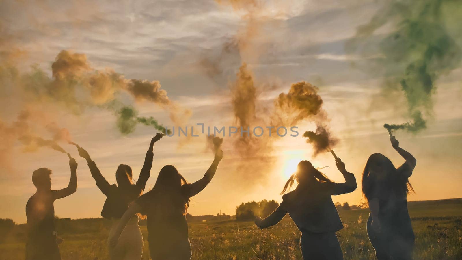 Happy friends girls waving colorful smoke at sunset